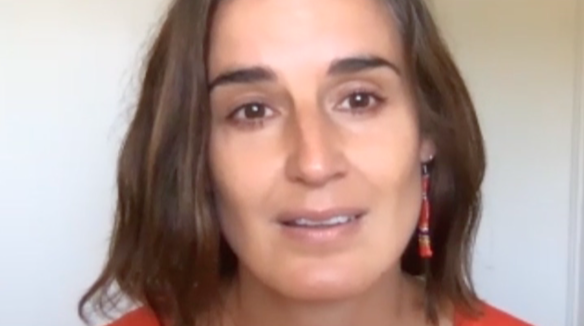 Close up of a woman looking sadly into the camera in front of a white wall