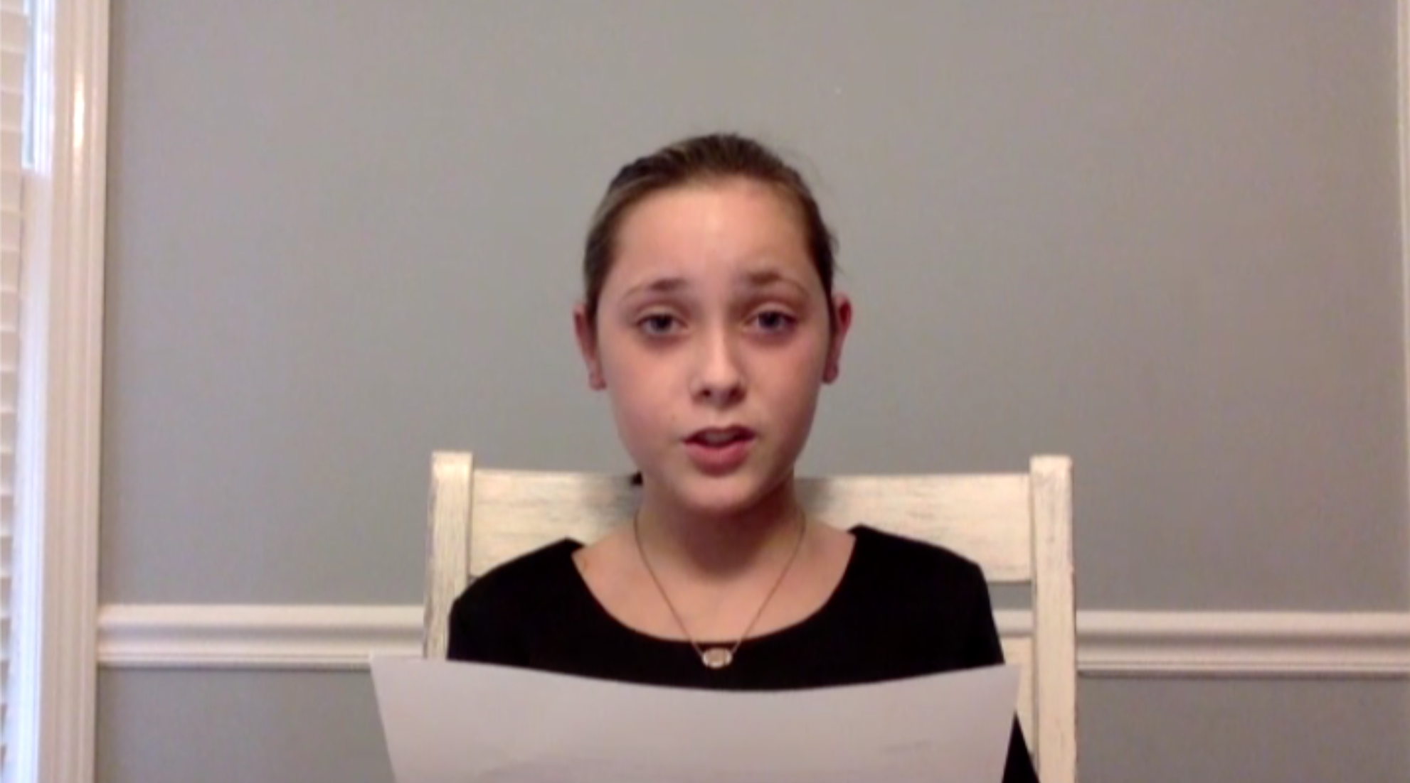 Young child longingly looking into the camera while sitting down and reading from a white piece of paper