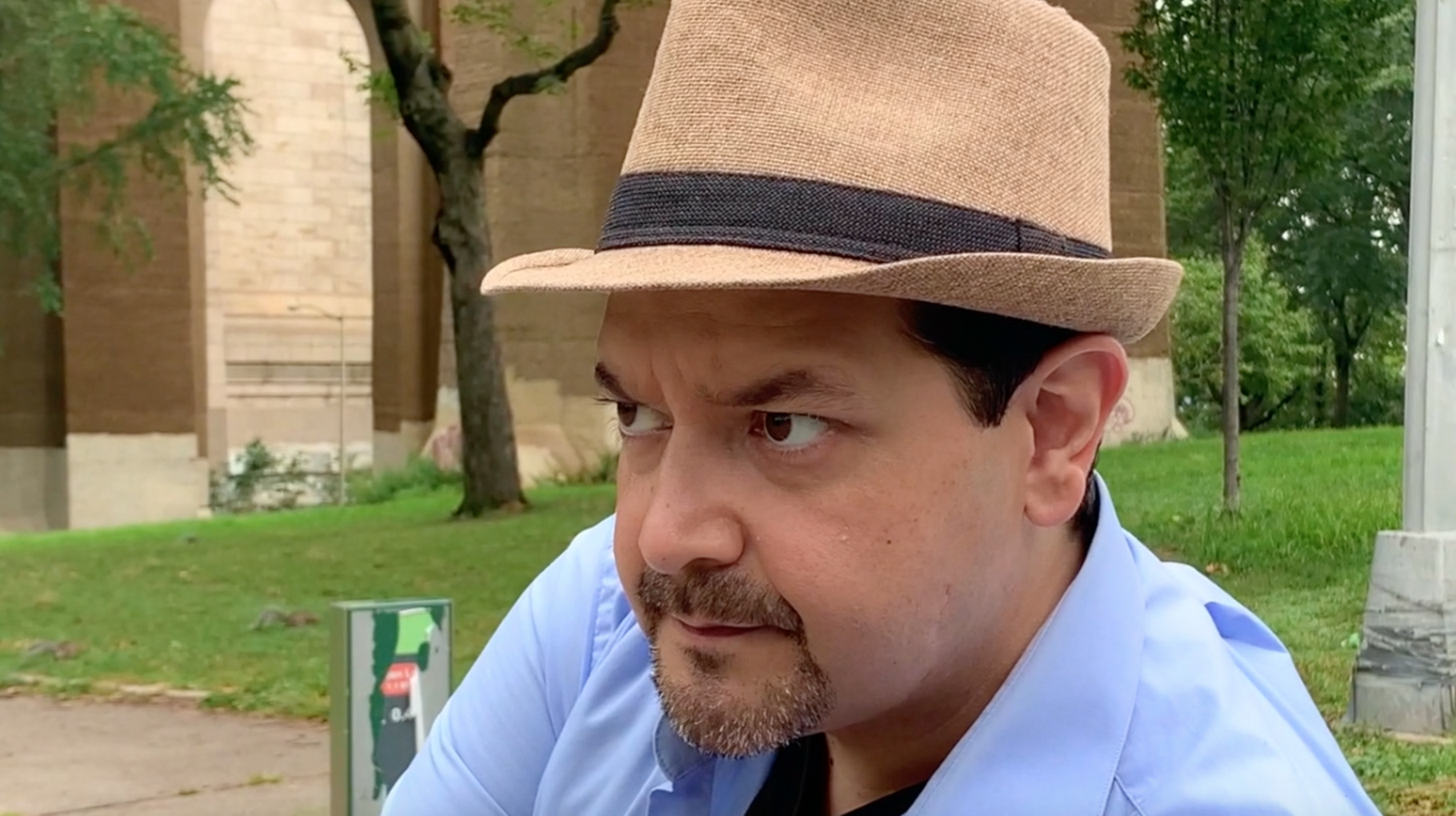 Close up of a man in a brown hat looking curiously into the distance while sitting on a park bench