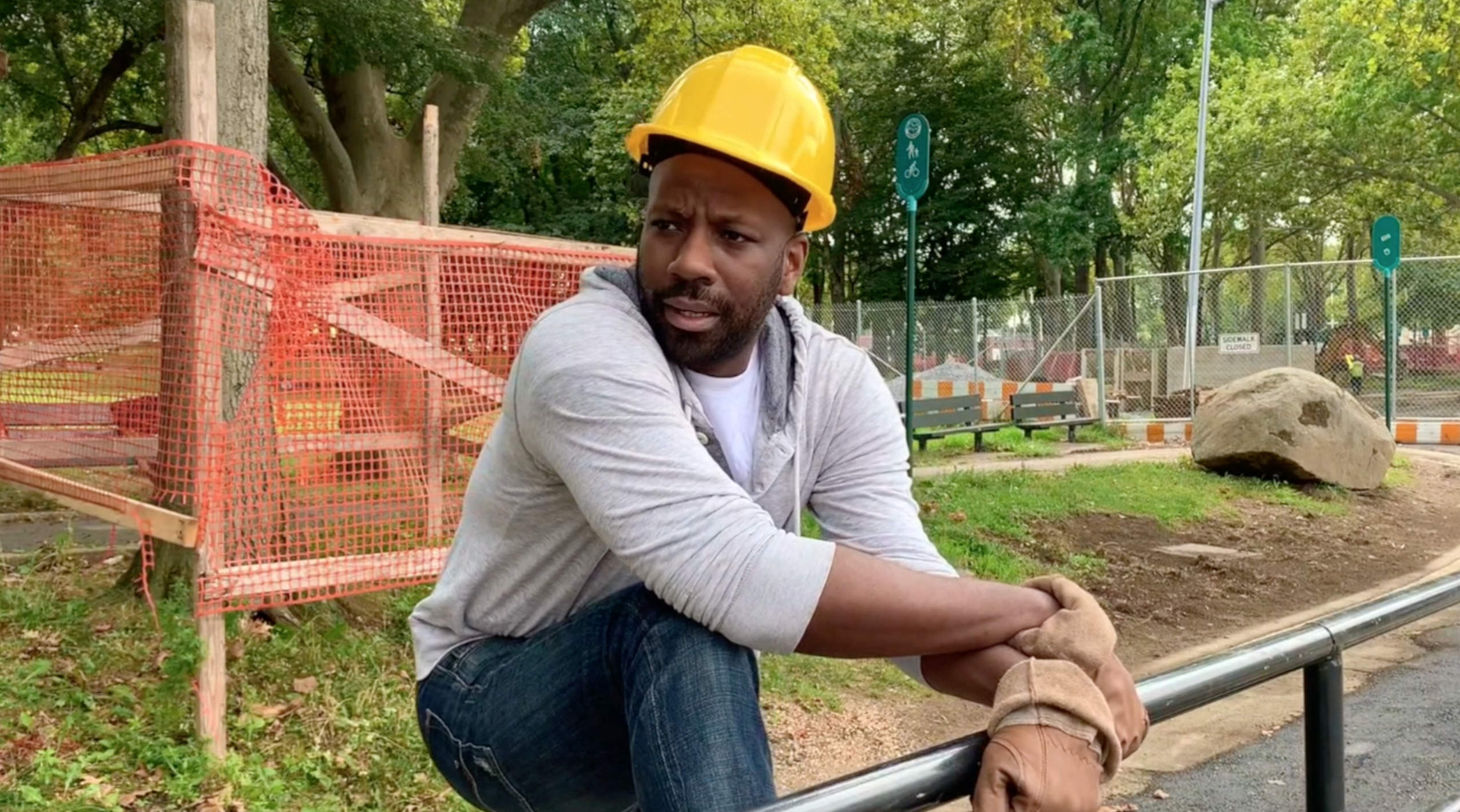Man wearing a hard hat in a construction zone leaning forward and grabbing onto a metal railing
