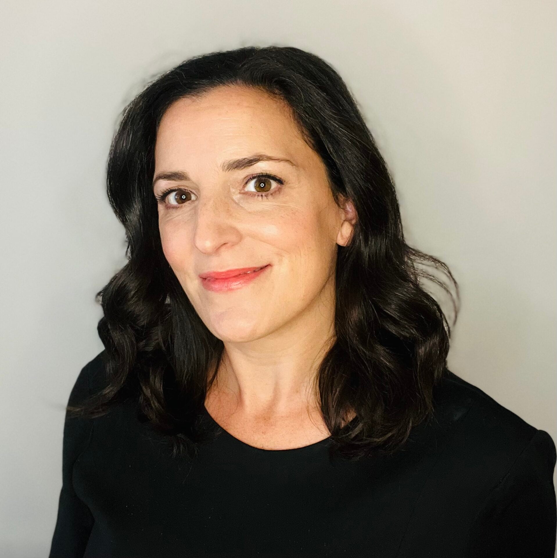 Lisa Tolin, associated with PEN America, is a woman with shoulder-length wavy dark hair and light skin, smiling slightly in a black top against a plain light gray background.