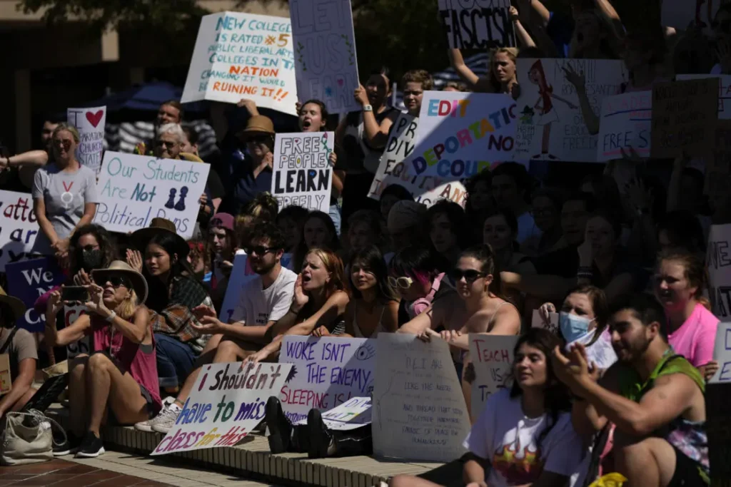 A large group of people are gathered outside, holding various protest signs. The diverse crowd is engaged in a rally or demonstration, with messages about education and political concerns. Many signs address Americas Censored Classrooms 2023, highlighting growing unrest over educational restrictions.