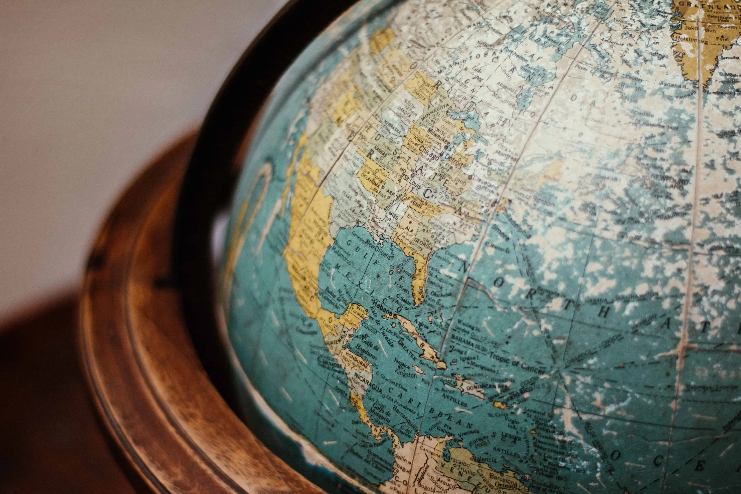 A close-up of a vintage globe showing North America, Central America, and parts of South America and the Atlantic Ocean, with faded colors and a wooden frame.