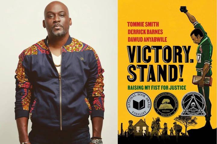 A man in a patterned jacket stands next to the cover of “Victory. Stand! Raising My Fist for Justice,” which features a man raising his fist, medals, and the authors’ names: Tommie Smith, Derrick Barnes, and Dawud Anyabwile.