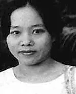 Black and white photo of a woman with dark hair pulled back, wearing a light-colored top and looking directly at the camera with a neutral expression.