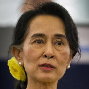 A woman with dark hair, a yellow flower and a pearl earring on her left ear, looks slightly to the side with a calm expression against a blurred background.