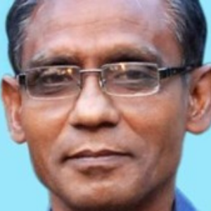 A middle-aged man with short, dark hair, wearing rectangular eyeglasses and a blue shirt, poses against a light blue background.