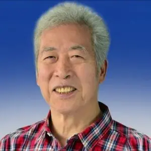 An older man with short gray hair smiles at the camera. He is wearing a red and blue plaid shirt, and the background is a smooth gradient from blue to light blue.