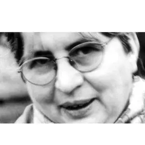 A black and white close-up photo of a person wearing round glasses and a scarf, looking slightly to the side with a neutral expression.