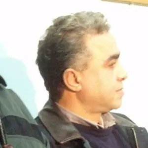 A man with short, gray hair is pictured in profile, wearing a dark jacket over a collared shirt and sweater, against a light background.