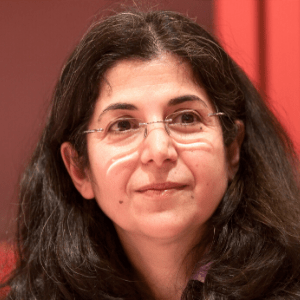 A woman with long dark hair and glasses is looking slightly to the side. She is in front of a red background and has a calm expression on her face.