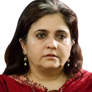 A woman with medium-length dark hair, wearing a maroon outfit with a patterned neckline and pearl drop earrings, looks ahead with a neutral expression on her face. The background is plain white.