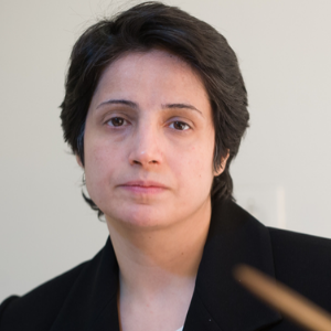 A person with short dark hair and a neutral expression is wearing a black jacket and looking slightly past the camera against a plain light background.