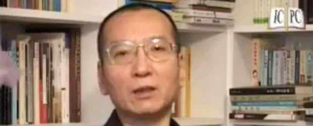 A person with short hair and glasses is in front of bookshelves filled with books. The background displays a variety of book spines, and part of a logo with the letters PC is visible, evoking the thoughtful presence of Liu Xiaobo.