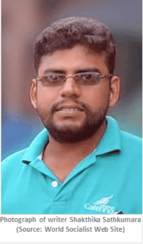 A man with short hair, a beard, and dark-rimmed glasses wears a teal collared shirt and stands outdoors, looking at the camera.