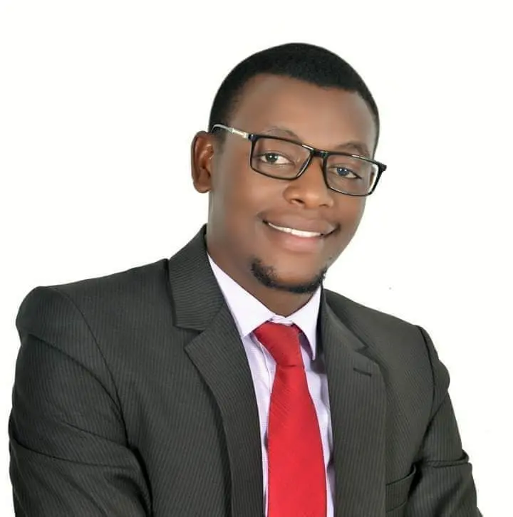 A man wearing glasses, a dark suit, white shirt, and red tie smiles at the camera against a plain white background.