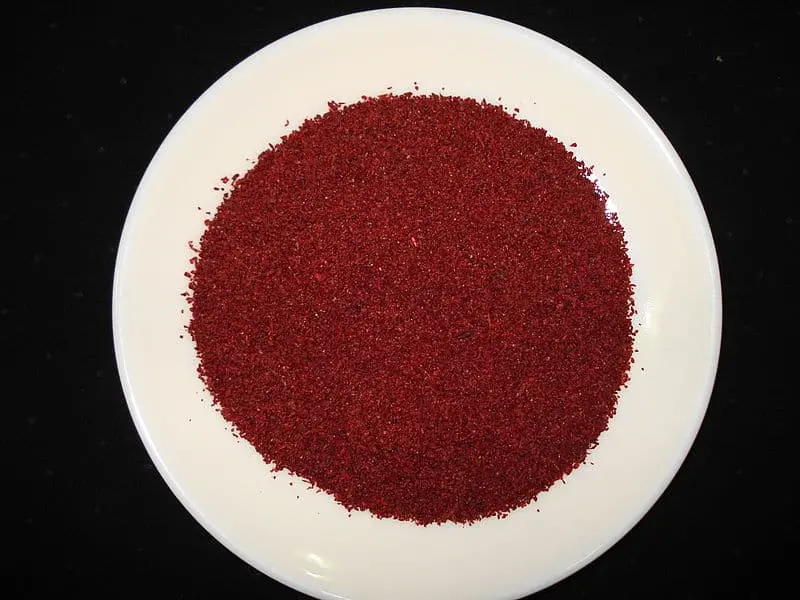 A white plate filled with a mound of finely ground, deep red spice, set against a black background.