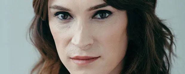A close-up of a person with long brown hair and fair skin, looking directly at the camera with a neutral expression against a plain background, subtly embodying the spirit of Banned Books Week.
