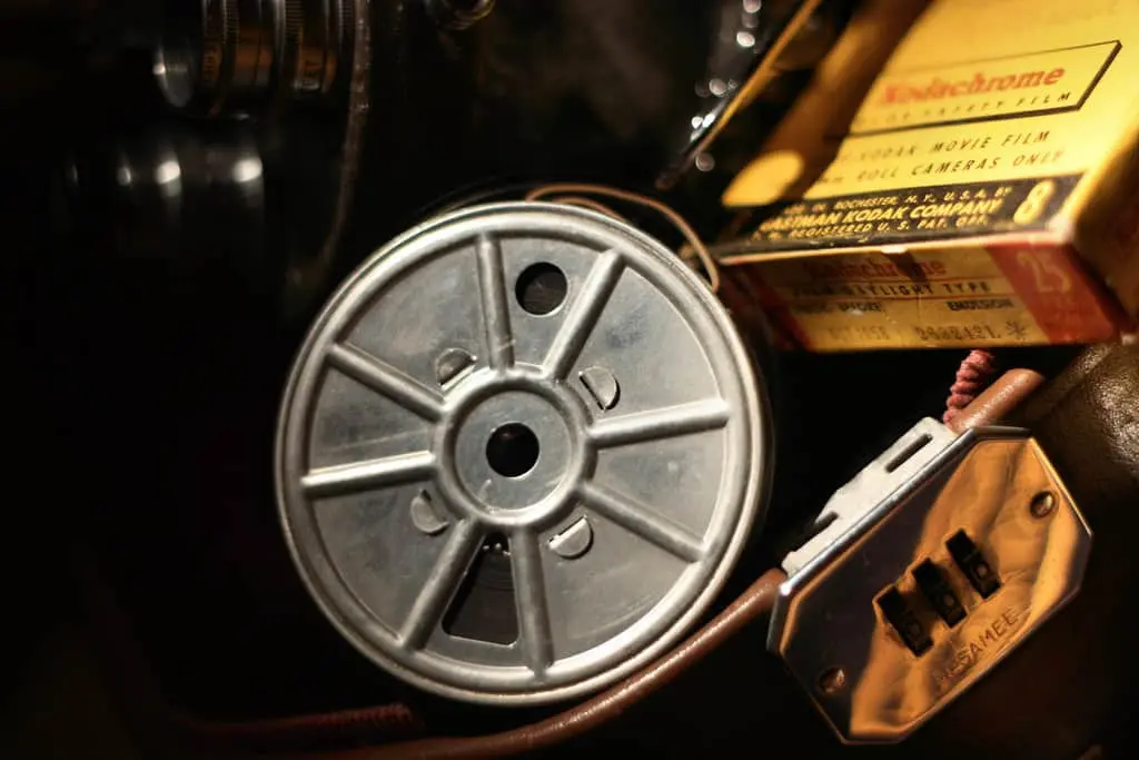 A close-up of a vintage metal film reel, an old electrical outlet, and a yellow Kodachrome movie film box—evoking the gritty atmosphere of prison writing—all placed on a dark surface.