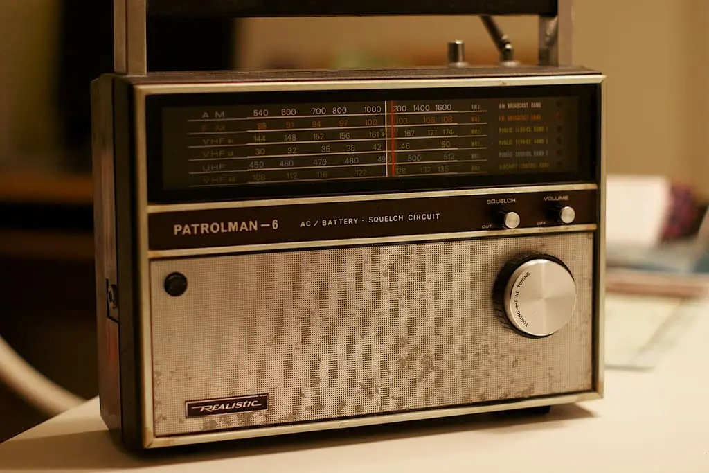 A vintage Patrolman-6 Realistic radio with a large tuning dial, volume knob, and frequency display sits on a table under warm lighting—an evocative scene that could inspire prison writing or creative reflection.