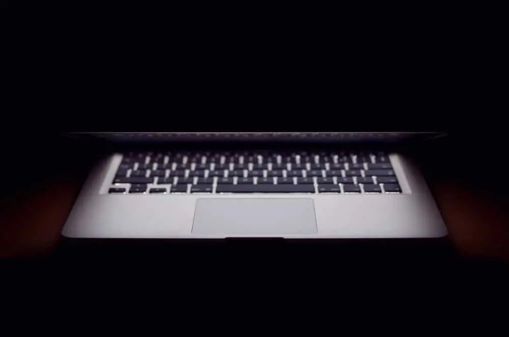 A laptop is partially open in a dark environment, with light illuminating its keyboard and trackpad while the screen remains mostly out of view.