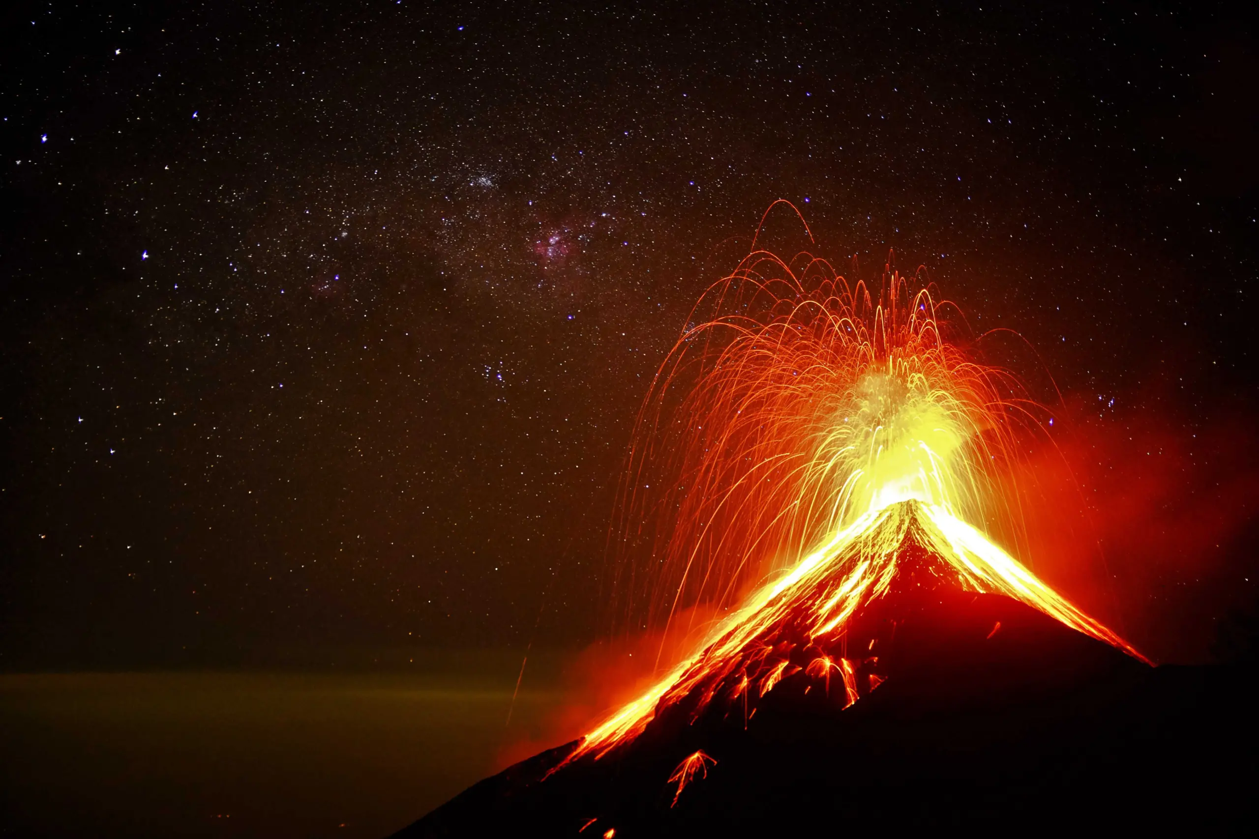 A volcano erupting at night, spewing bright orange lava and ash into the sky, with a backdrop of dark sky filled with stars.