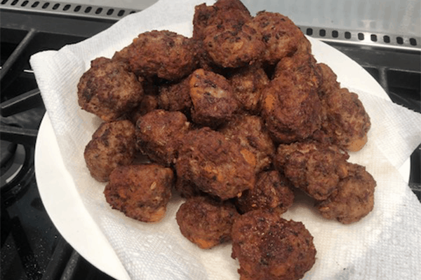 A plate lined with paper towels holds a pile of browned, crispy meatballs, freshly cooked and draining excess oil. The plate is on a stovetop.