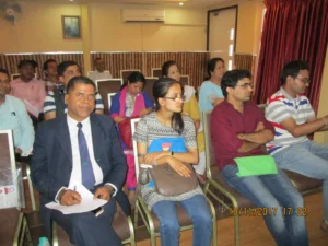 A group of people, including men and women, are seated in rows at a PEN Nepal seminar room on 10/11/2017, attentively listening. One man in a suit holds papers, while others sit casually dressed.