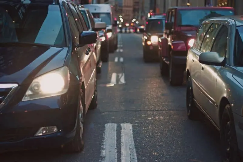 Cars stuck in heavy traffic on a city street, with headlights on and vehicles close together, suggesting congestion during early morning or evening hours.