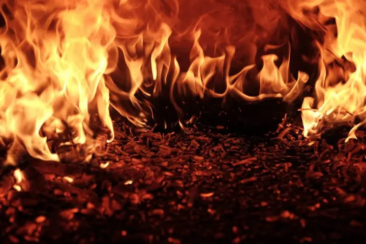 Bright orange flames burn intensely over a bed of dark wood chips, creating a dramatic scene of fire and heat.