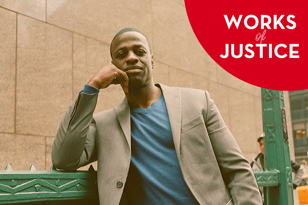 A man in a light gray suit and blue shirt leans on a green railing outdoors, smiling slightly. In the top right corner, a red circle displays the text WORKS of JUSTICE in white letters.