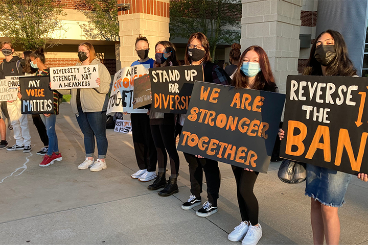 A group of people stand outside holding signs supporting diversity and opposing a book ban. The signs read messages like “We are stronger together,” “Stand up for diversity,” and promote access to Book Ban Resources.