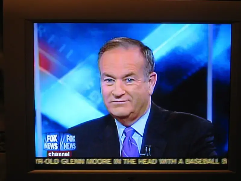 A man in a suit and purple tie appears on a Fox News channel broadcast. The lower screen shows a news ticker with partial text that reads, OLD GLENN MOORE IN THE HEAD WITH A BASEBALL.