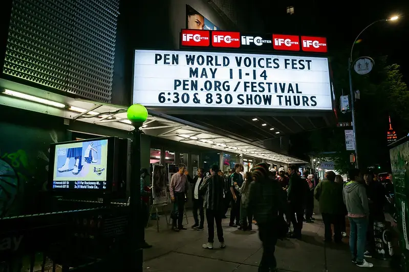 A crowd gathers outside a theater at night under a marquee advertising the PEN World Voices Fest—an event about PEN America—taking place May 11-14, with showtimes at 6:30 and 8:30 PM on Thursday. The venue is lit and busy.