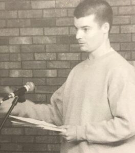 B. Batchelor reads his work in front of a microphone