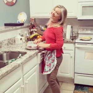 Shawna Kenney in her kitchen, smiling at the camera and simultaneously crimping a pie crust