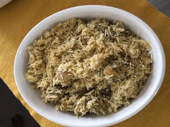 A white oval dish filled with seasoned rice and pieces of vegetables or meat, placed on a yellow textured placemat, showcases Jehan Nizar cooking inspiration.