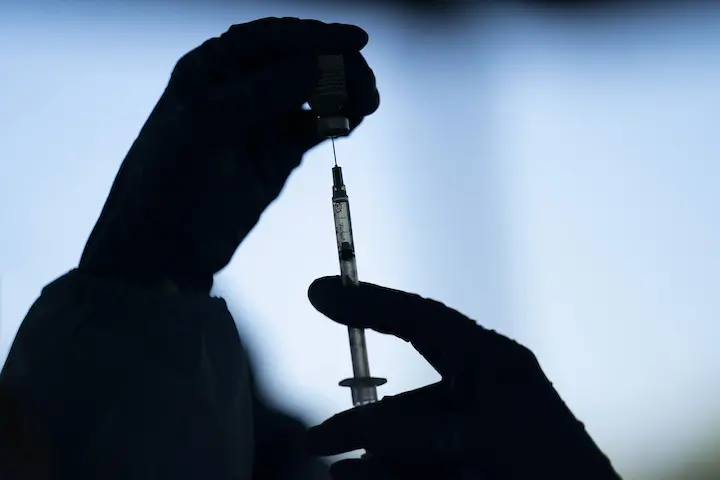 Silhouette of gloved hands preparing a syringe with a vaccine from a vial, set against a blurred blue background, highlighting the importance of combating vaccine misinformation in communities of color.