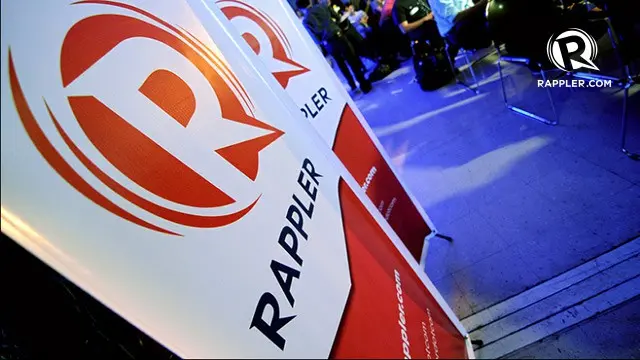 Banners with the red and white Rappler logo and text stand in the foreground at an event, with people seated in the blue-lit background. The Rappler website is visible in the top right corner.