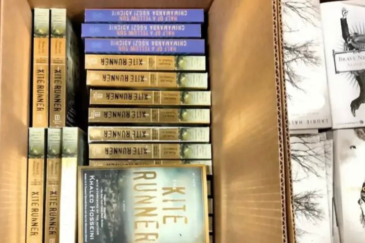 Stacks of the Khaled-Hosseini-banned-book The Kite Runner are arranged neatly in a box. Next to them are copies of another book with a white cover, possibly Brave Enough by Cheryl Strayed.