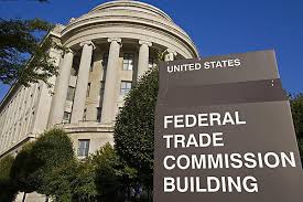 A large sign reading United States Federal Trade Commission Building stands in front of a grand, columned government building surrounded by trees under a clear blue sky.