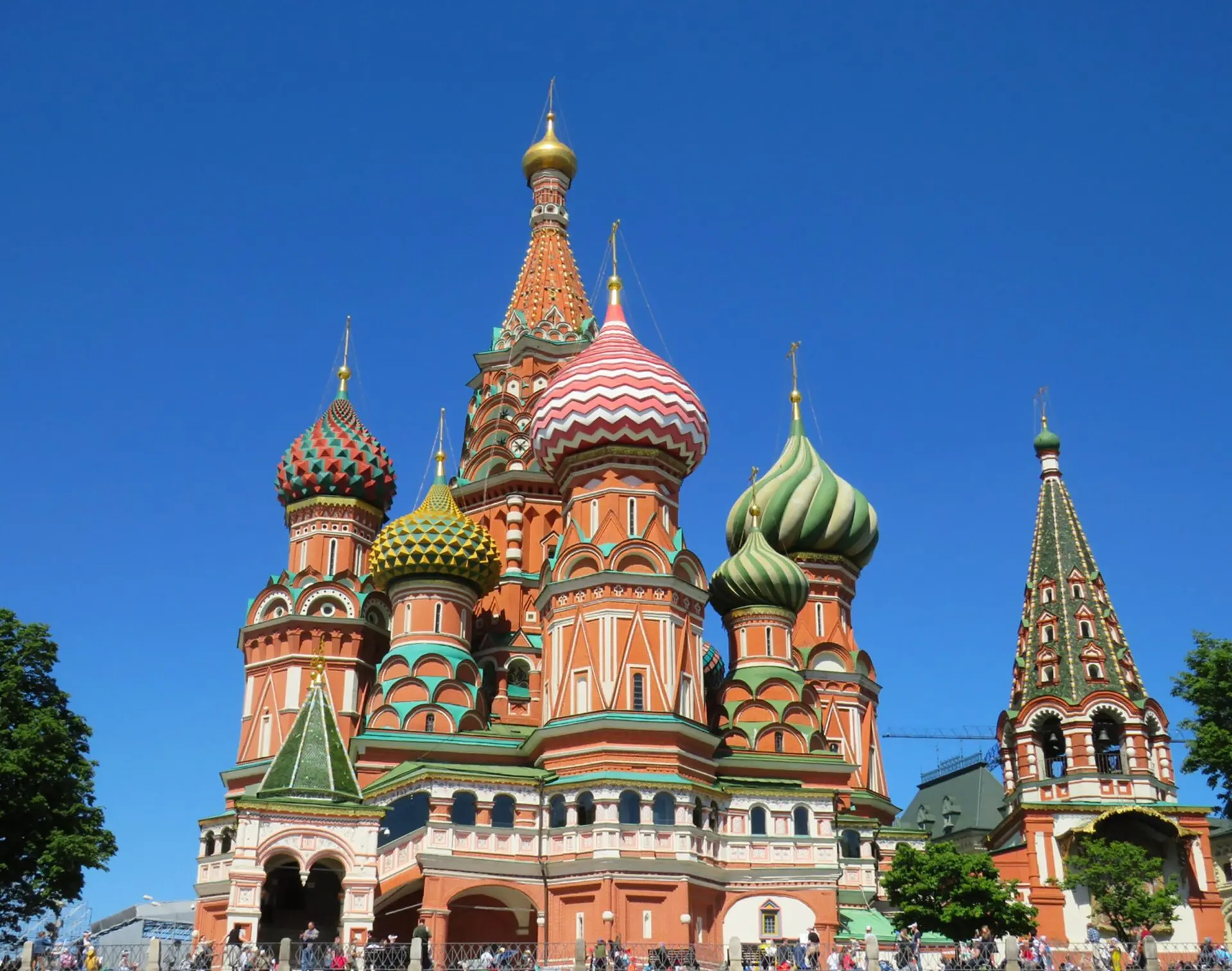 St. Basil’s Cathedral in Moscow with its colorful, onion-shaped domes stands under a clear blue sky. Tourists are visible at the base of the cathedral, highlighting its grand and intricate architecture.