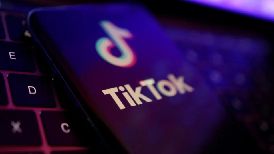 A smartphone displaying the TikTok logo rests on a laptop keyboard, with colorful reflections highlighting the TikTok branding on the phone’s screen.