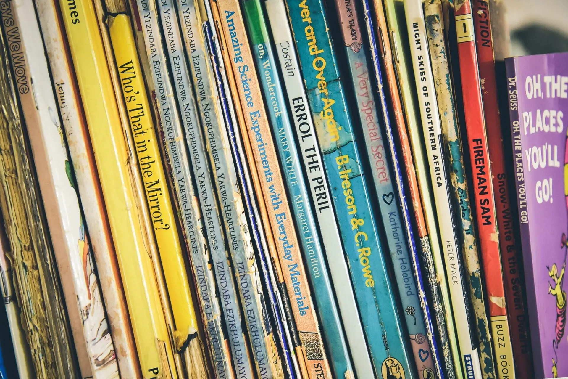 Close-up of a bookshelf filled with childrens books, showing colorful spines and various titles, including “Who’s That in the Mirror?”, “Experiments with Everyday Materials,” and “Oh, the Places Youll Go!” among others.