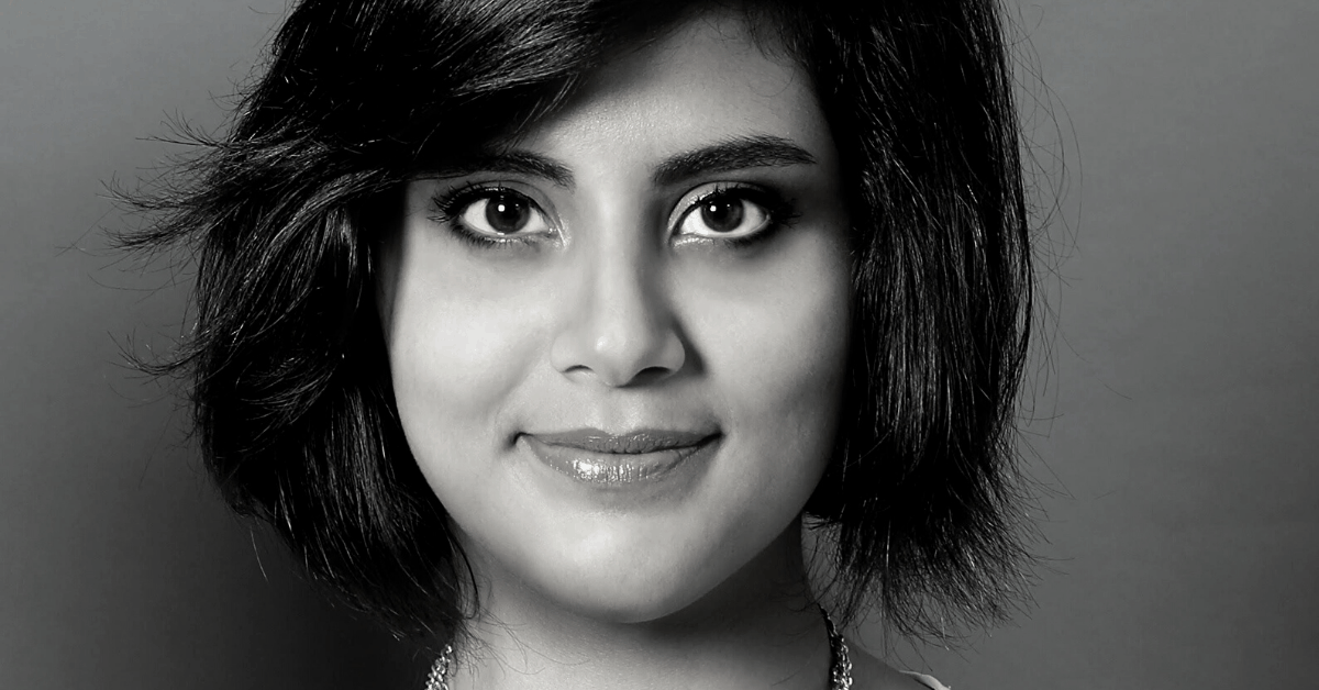 A black and white portrait of a young woman with short, dark hair, wide eyes, and a slight smile, looking directly at the camera against a plain background.