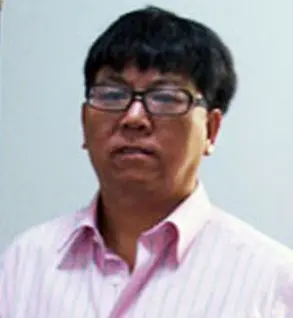 A person wearing glasses and a light pink, striped collared shirt stands in front of a plain, light-colored background.