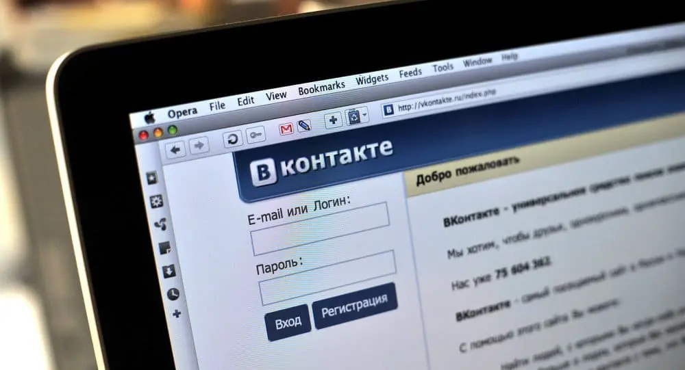 A computer screen displays the VKontakte login page in Russian, with fields for email or login and password, as well as buttons for login and registration, viewed in the Opera web browser.