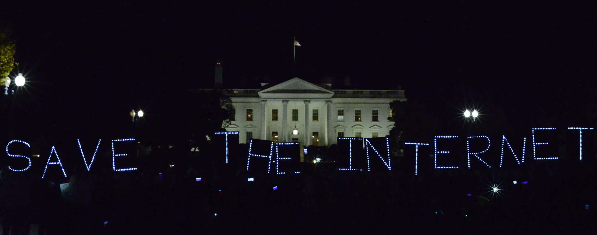 People hold illuminated signs spelling “SAVE THE INTERNET” at night in front of the White House, advocating for internet freedom.