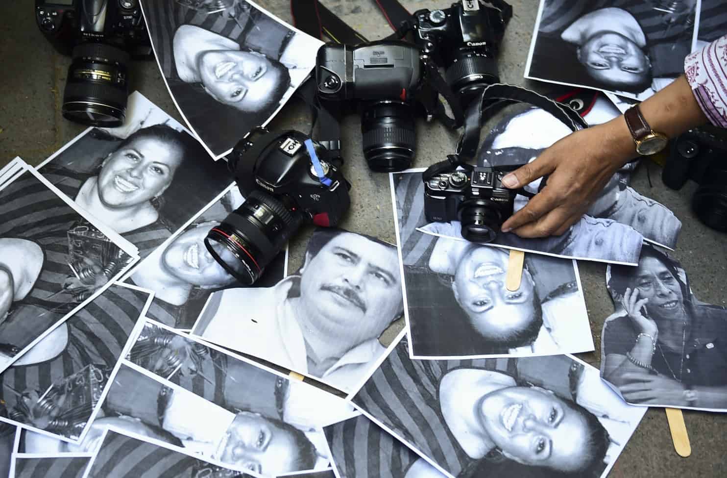 Black-and-white portraits of people are scattered on the ground among several cameras, while a person’s hand holds a smaller camera over the photos.