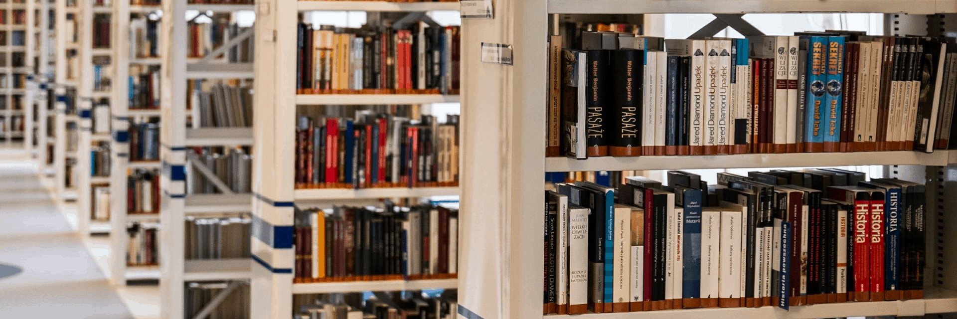Rows of bookshelves filled with various books in a well-lit library, with book spines facing outward and organized neatly on the shelves.